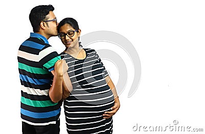 a young couple showing a pregnant lady in satisfied content expression with her husband kissing ger head in white background with Stock Photo