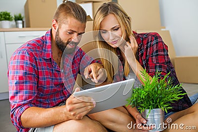 Young couple sitting on the floor with tablet pc and choosing furniture to their new apartment. Stock Photo