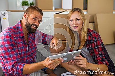 Young couple sitting on the floor with tablet pc and choosing furniture to their new apartment. Stock Photo