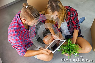 Young couple sitting on the floor with tablet pc and choosing furniture to their new apartment. Stock Photo