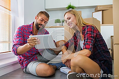 Young couple sitting on the floor with tablet pc and choosing furniture to their new apartment. Stock Photo