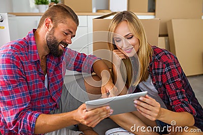 Young couple sitting on the floor with tablet pc and choosing furniture to their new apartment. Stock Photo