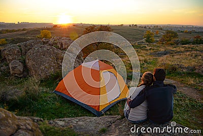 Young Couple Sitting near Tent and Watching Beautirul Sunset in the Mountains. Adventure and Family Travel. Stock Photo