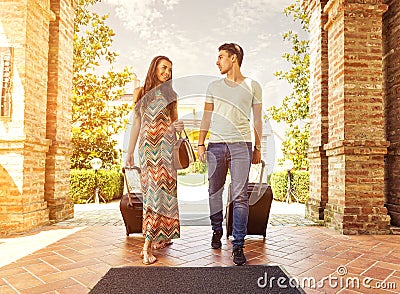 Young couple standing at hotel corridor upon arrival, looking for room, holding suitcases Stock Photo