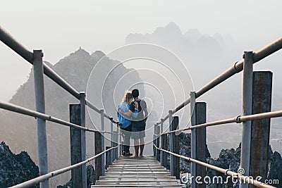 Young couple standing on mountain peak with stairs going down during sunrise foggy morning in Hpa-An, Myanmar Stock Photo