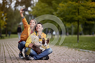 Young couple taking selfie with their dog in a lap, sitting on a path in park Stock Photo