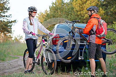 Young Couple Unmounting Mountain Bikes from Bike Rack on the Car. Adventure and Family Travel Concept. Stock Photo