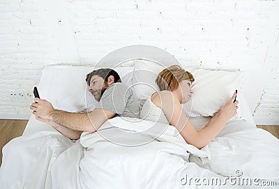 Young couple using mobile phone in bed ignoring each other in relationship communication problems Stock Photo