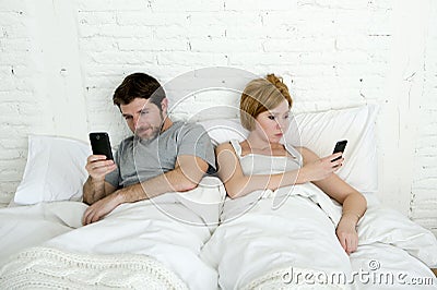 Young couple using mobile phone in bed ignoring each other in relationship communication problems Stock Photo