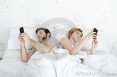 Young couple using mobile phone in bed ignoring each other in relationship communication problems Stock Photo