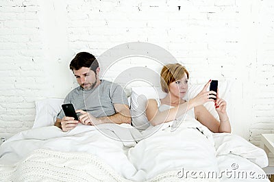 young couple using mobile phone in bed ignoring each other in relationship communication problems Stock Photo