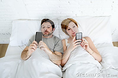 young couple using mobile phone in bed ignoring each other in relationship communication problems Stock Photo