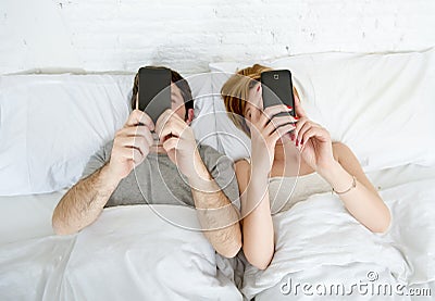 young couple using mobile phone in bed ignoring each other in relationship communication problems Stock Photo