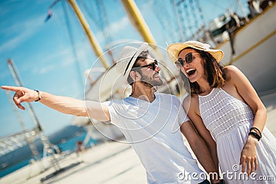 Young couple walking by the harbor of a touristic sea resort with sailboats on background Stock Photo