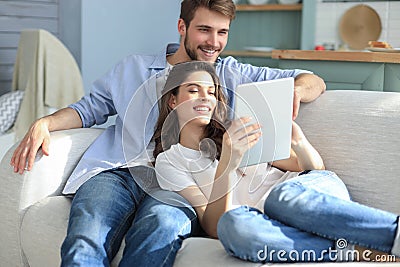 Young couple watching media content online in a tablet sitting on a sofa in the living room Stock Photo