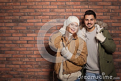 Young couple wearing warm clothes against wall, space for text. Ready for winter vacation Stock Photo