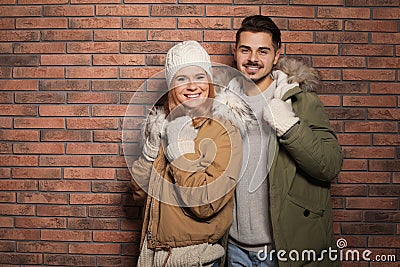 Young couple wearing warm clothes against wall, space for text. Ready for winter vacation Stock Photo