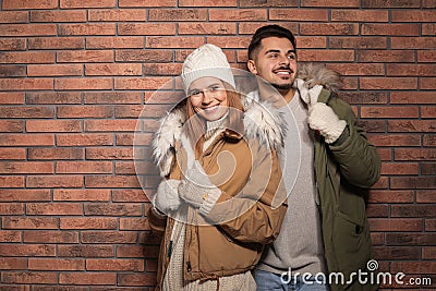 Young couple wearing warm clothes against wall, space for text. Ready for winter vacation Stock Photo