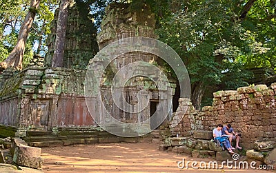 Young couple of western tourists resting by the ruins of Ta Prohm temple in Angkor, Cambodia. Editorial Stock Photo