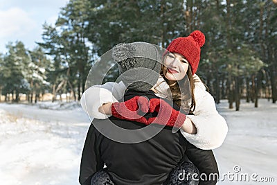 Young couple on winter forest background, girl keeps hands in heart shape sign. Winter sunny day Stock Photo