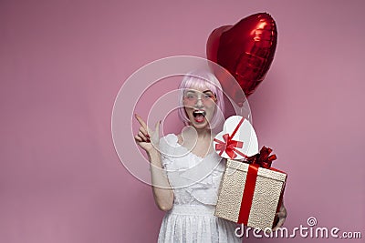 Young crazy girl with pink hair in a dress holds gifts and inflatable balls and screams Stock Photo