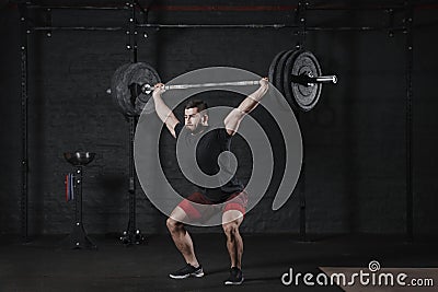 Young crossfit athlete lifting barbell overhead at gym. Man practicing functional training powerlifting workout exercises Stock Photo