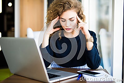 Young curly businesswoman suffering from headache in front of laptop at office desk in modern office Stock Photo