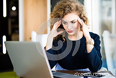 Young curly businesswoman suffering from headache in front of laptop at office desk in modern office Stock Photo