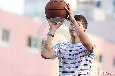 Young cute boy plays basketball at the outdoor streetball court on a sunny summer day. Teenager player in action dribbling Stock Photo