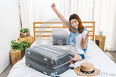 Young cute happy Asian girl finished packing suitcase luggage on bed in bedroom, ready to go abroad solo trip Stock Photo