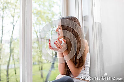 Young and cute lady sitting on the windowsill and looking out th Stock Photo