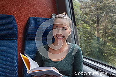 Young cute woman smiling and reading a book while travelling by train Stock Photo