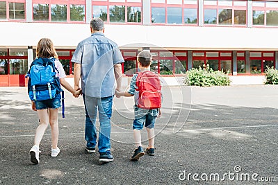 A young dad leads his children by the hand with backpacks on their backs to school. Back to school. Beginning of the Stock Photo