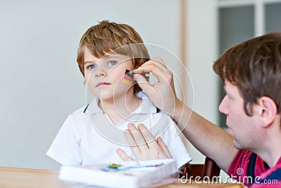 Young dad painting flag on face of little son for football or soccer game. Happy excited preschool kid boy fan and Stock Photo