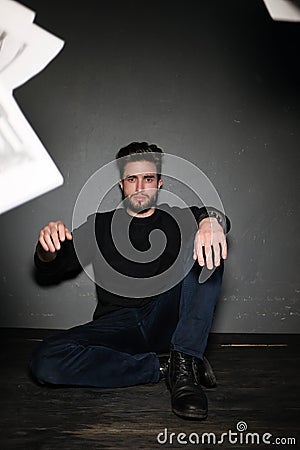 A young dark-haired man with a beard sits on the floor and throws papers and documents into the air. Human emotions Stock Photo