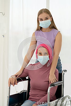 Young daughter embracing her sick mom who wearing headscarf on wheelchair, giving support battling through cancer Stock Photo