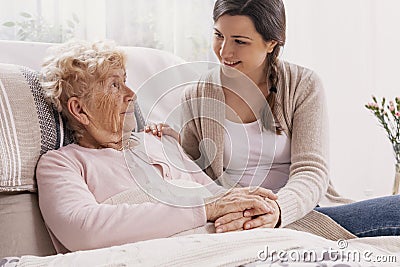 Young daughter supporting sick mother lying in hospital bed Stock Photo