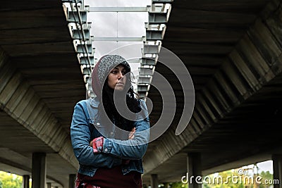 Young depressed homeless girl or woman standing alone under the bridge on the street on the cold weather feeling anxious abandoned Stock Photo