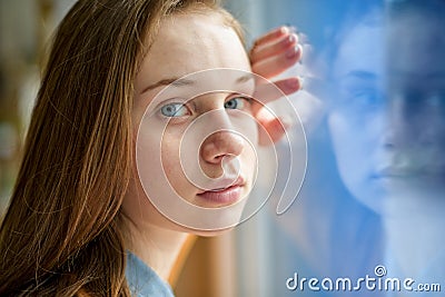 Young depressed lonely female college student standing by a window at her school, looking at the camera. Bullying concept. Stock Photo