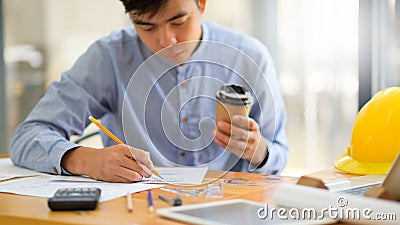 Young designer with a take away coffee mug in hand is using a pencil to sketch a house design Stock Photo