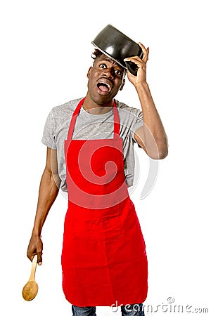 Young desperate and confused black afro american man in chef apron holding cooking pot in his head Stock Photo