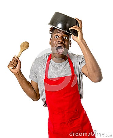 Young desperate and confused black afro american man in chef apron holding cooking pot in his head Stock Photo