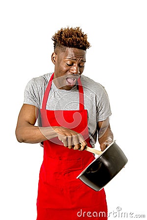 Young desperate and confused black afro american man in chef apron holding cooking pot and spoon in his hands looking lost Stock Photo