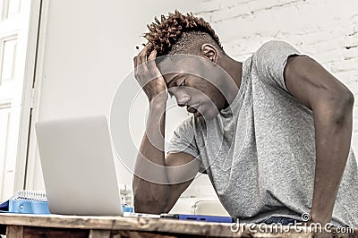 Young desperate and overwhelmed black afro American student man in stress at home working stressed with laptop computer worried an Stock Photo