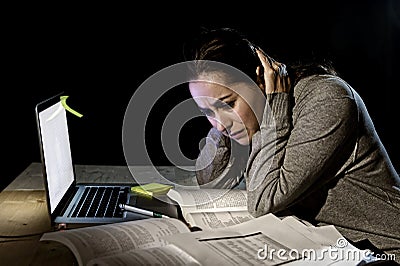 Young desperate university student girl in stress for exam studying with books and computer laptop late at night Stock Photo