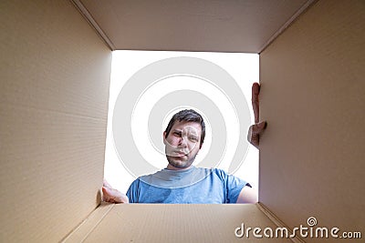 Young disappointed man is looking on gift inside cardboard box Stock Photo