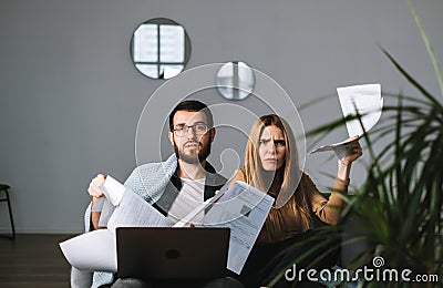 Young dissatisfied couple manages finances with laptop, looking through their bank accounts in the living room on the sofa Stock Photo