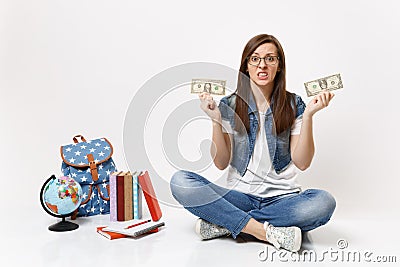 Young dissatisfied woman student hold dollar bills cash money feeling stressed by lack of money sit near globe backpack Stock Photo