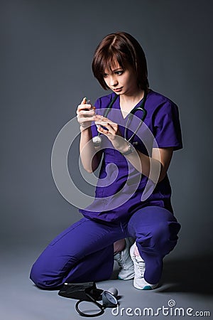 A young doctor in a blue coat on a gray background holds in his hand a syringe with medicine. Medical worker Stock Photo