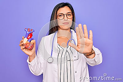 Young doctor cardiology specialist woman holding medical heart over pruple background with open hand doing stop sign with serious Stock Photo